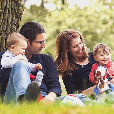 Two parents each holding a toddler sitting outside